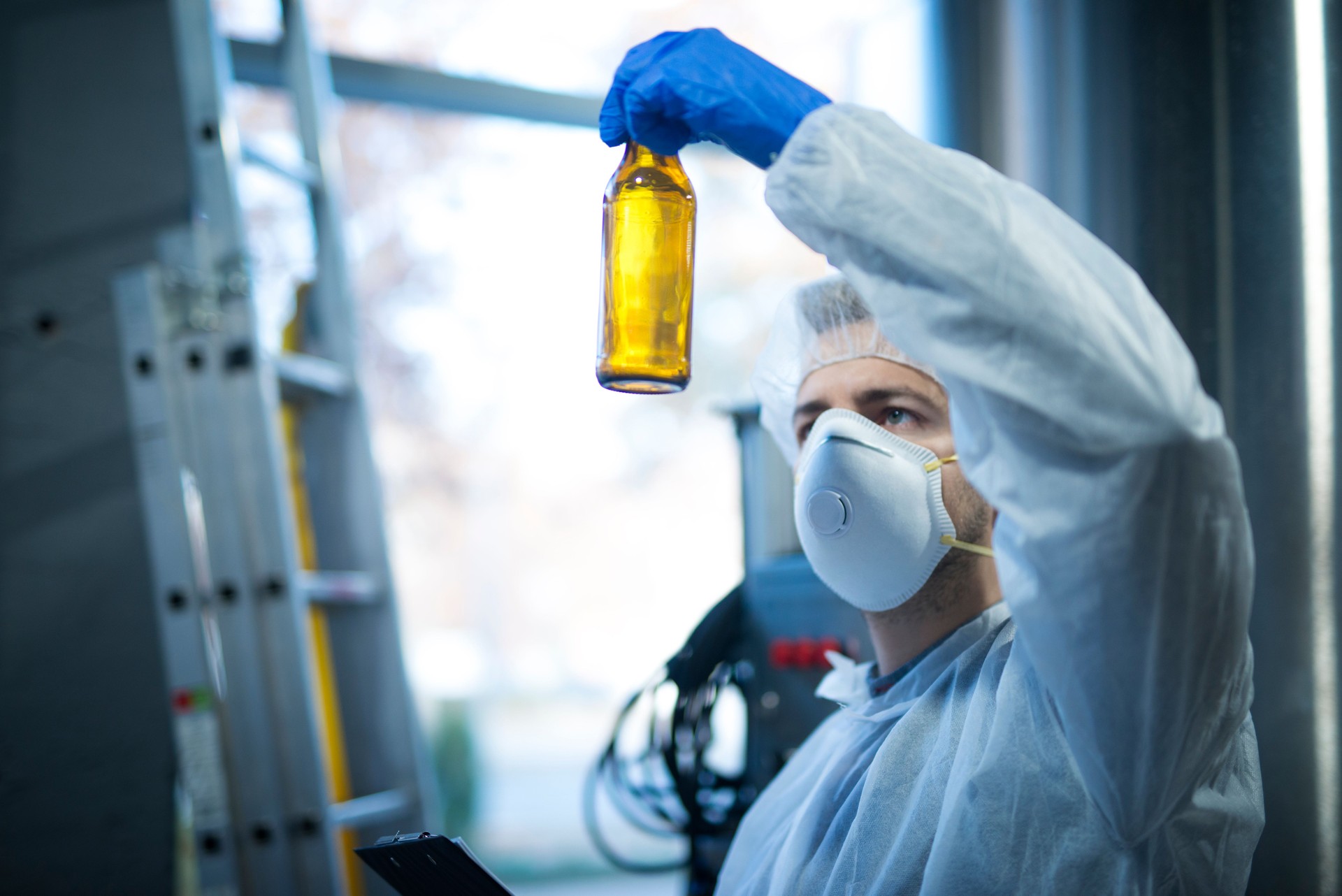 Technologist expert in beer production factory holding glass bottle and checking quality. Food and beverage quality control.